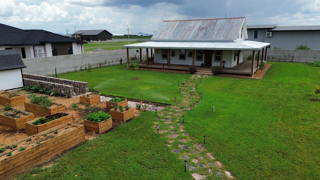 Aerial view of the restored 1922 house, wraparound porch, stone path and kitchen garden