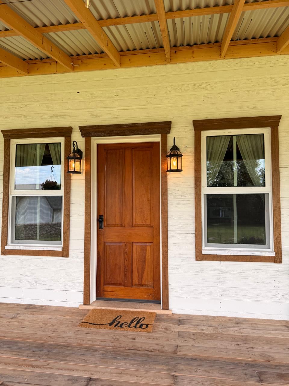 Wood entry door with a 'hello' mat on the plank porch floor