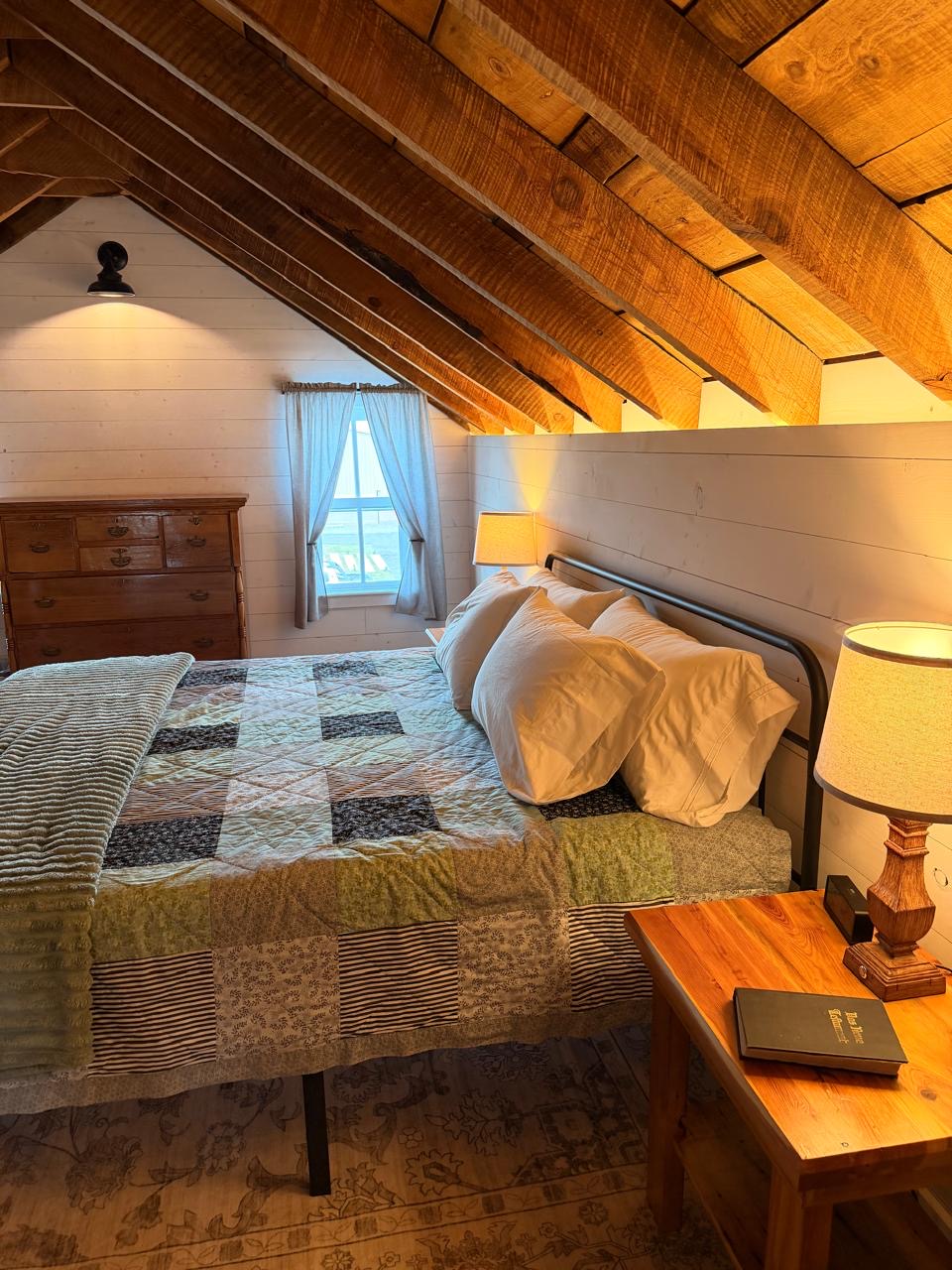 Bed made with a patchwork quilt under the exposed rafters