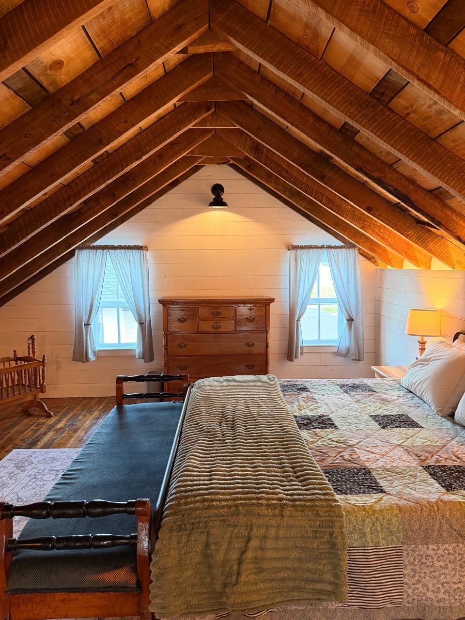 Attic bedroom beneath the original timber-beam roof with a patchwork quilt and antique dresser