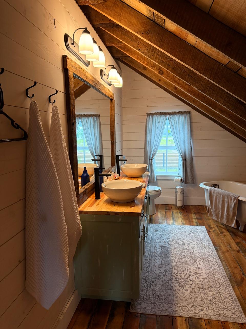 Attic bathroom with a clawfoot tub and double vessel sinks under the eaves