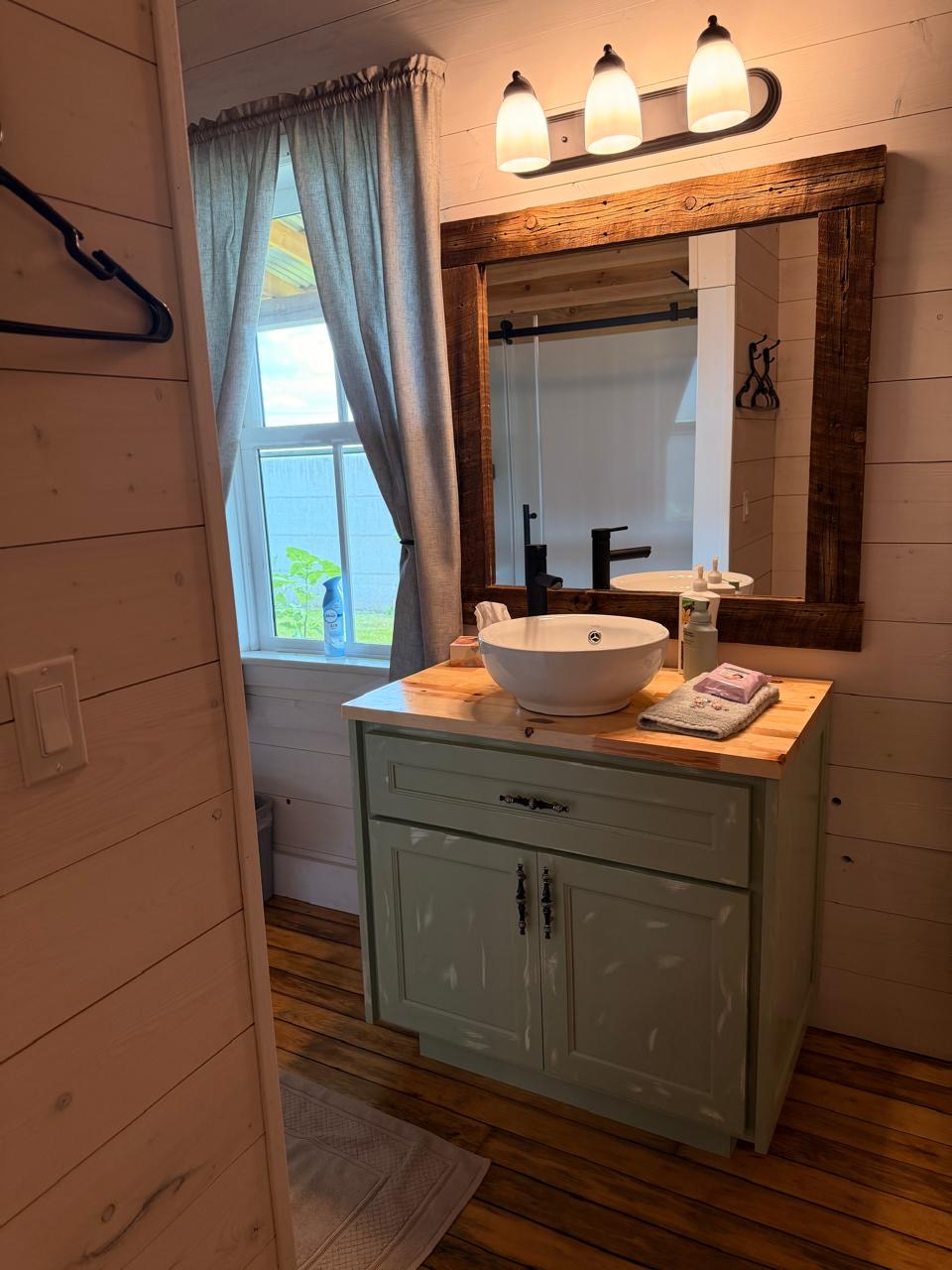 Small bathroom with a sage-green vanity and reclaimed-wood mirror by the window
