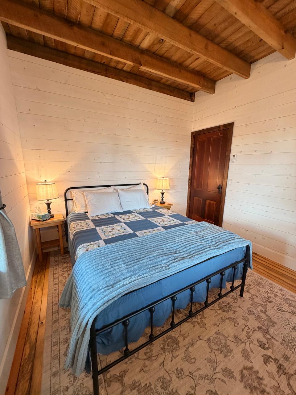 Bedroom with a black iron bed, blue quilt and a wood panel door