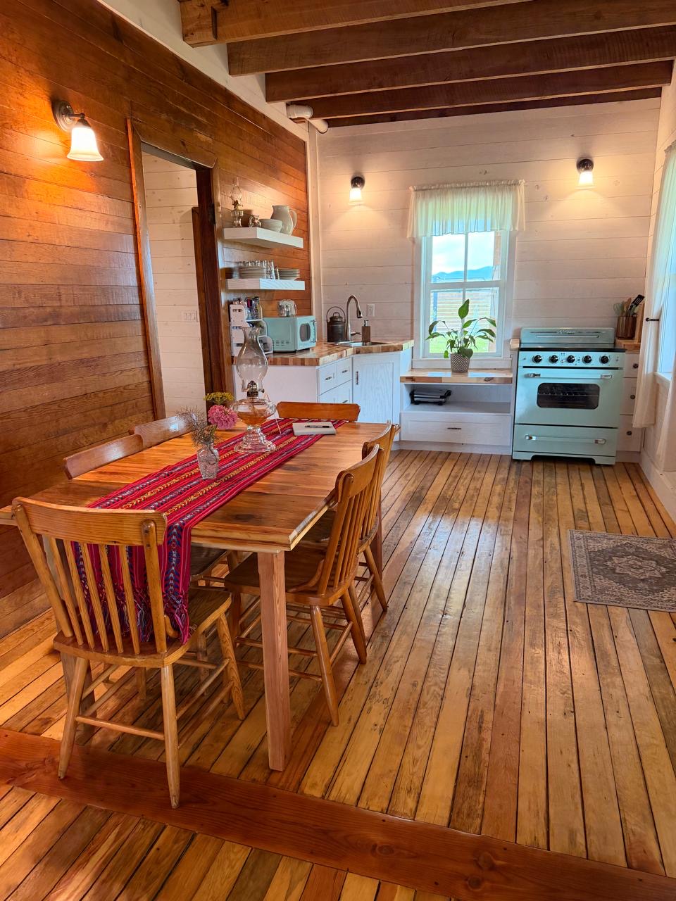 Dining table with a woven textile runner and oil lamp beside the kitchen